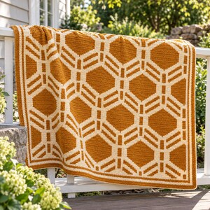 May include: A rectangular crochet blanket featuring a repeating geometric pattern in mustard yellow and cream white. The design consists of interconnected hexagonal shapes with a thick, solid border in the same two-tone color scheme.