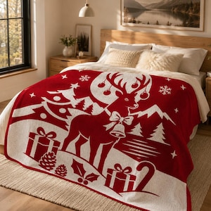 Pode incluir: Uma manta vermelho-escura e branca com um grande gr&aacute;fico de uma rena com uma coleira de sino, rodeada por pinheiros, caixas de presente, flocos de neve e folhas de azevinho. O design inclui ornamentos pendurados nas hastes da rena.