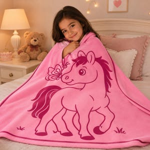 May include: A pink hooded blanket with a cartoon horse and butterfly design. The blanket is made of a soft, plush material. The horse is light pink with a dark pink mane and tail. The butterfly is dark pink. Ideal for children.