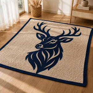 May include: A rectangular rug with a tan background and a navy blue deer head design. The deer has large antlers and a detailed face. The rug has a navy blue border, and is made of a woven material.