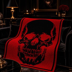 Puede incluir: Una manta roja y negra con estampado de calavera sobre un sof&aacute; negro. La manta presenta un gran dise&ntilde;o de calavera negra sobre un fondo rojo. El tejido tiene un borde negro y est&aacute; hecho de un material de punto suave.