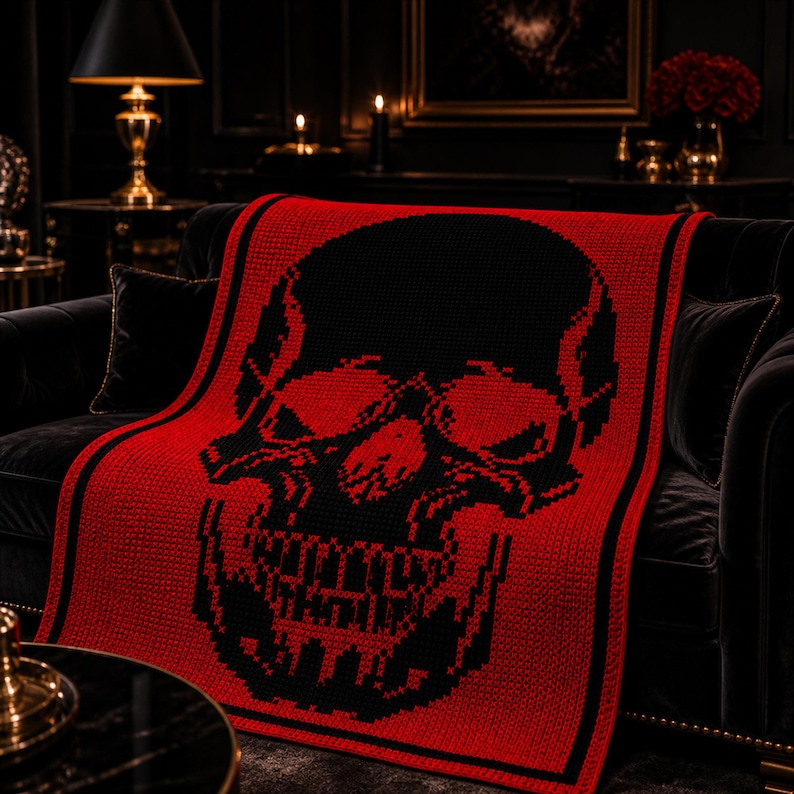 Puede incluir: Una manta roja y negra con estampado de calavera sobre un sof&aacute; negro. La manta presenta un gran dise&ntilde;o de calavera negra sobre un fondo rojo. El tejido tiene un borde negro y est&aacute; hecho de un material de punto suave.