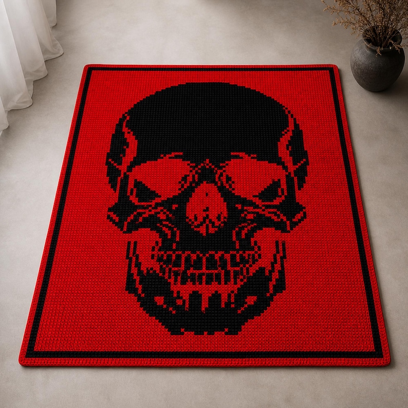 Puede incluir: Una manta de ganchillo roja y negra con un dise&ntilde;o de calavera. La calavera negra est&aacute; centrada sobre el fondo rojo. La manta tiene un borde negro. Los rasgos de la calavera son detallados, incluyendo cuencas de los ojos, nariz y dientes.