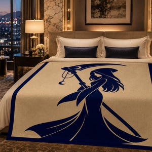 May include: A cream-coloured bed blanket featuring a dark blue border and a large, centred graphic of a hooded figure holding a scythe. The figure has long hair and is depicted in a silhouette style, with a crescent moon detail on the scythe blade.