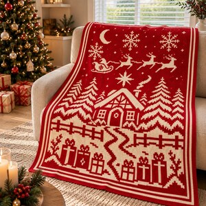 May include: A rectangular knit throw blanket featuring a red and cream holiday pattern. The design displays a winter scene with a cabin, pine trees, a fence, wrapped gifts, a crescent moon, snowflakes, and a sleigh pulled by reindeer.