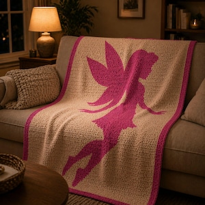 May include: A beige crocheted blanket with a magenta fairy silhouette. The blanket has a magenta border and is draped over a sofa. The room is dimly lit with a lamp and a side table.