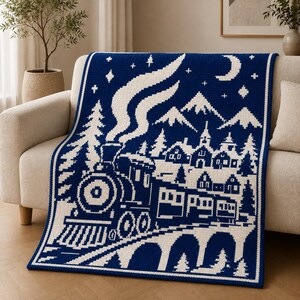 May include: A rectangular crochet blanket featuring a dark blue and white pixelated design of a steam locomotive traveling across a bridge. The scene includes a snowy village, pine trees, mountain peaks, a crescent moon, and stars in the night sky.