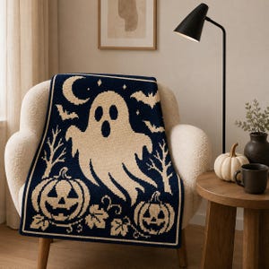 May include: A dark navy blue and cream knit throw blanket featuring a large central ghost, two jack-o'-lantern pumpkins, bare trees, bats, and a crescent moon. The design is rendered in a repeating pixelated pattern across the rectangular fabric.