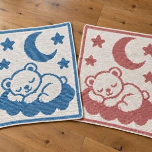 May include: Two rectangular crochet blankets featuring a sleeping bear on a cloud, a crescent moon, and stars. One blanket has a cream base with blue accents, and the other has a cream base with dusty rose accents, both with matching borders.