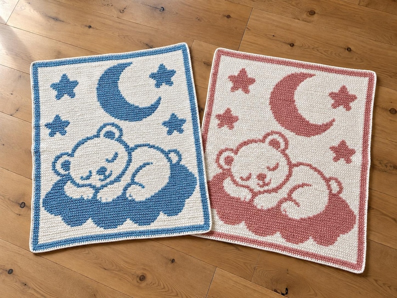 May include: Two rectangular crochet blankets featuring a sleeping bear on a cloud, a crescent moon, and stars. One blanket has a cream base with blue accents, and the other has a cream base with dusty rose accents, both with matching borders.