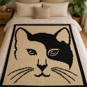 May include: A large, rectangular crochet blanket featuring a cat face design. The cat's face is divided into black and cream-colored sections, with black outlining the face and a black border. The blanket is displayed on a bed with white bedding.