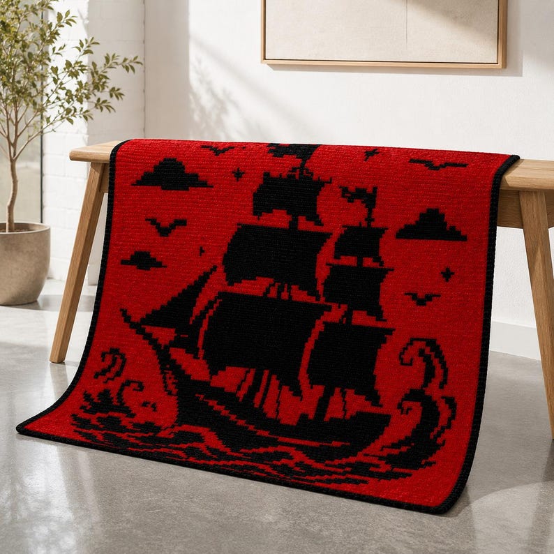 May include: A rectangular throw blanket featuring a vibrant red background with a black pixelated graphic of a sailing ship on the ocean. The design includes black silhouettes of clouds, birds, and stars surrounding the ship, with a black border.