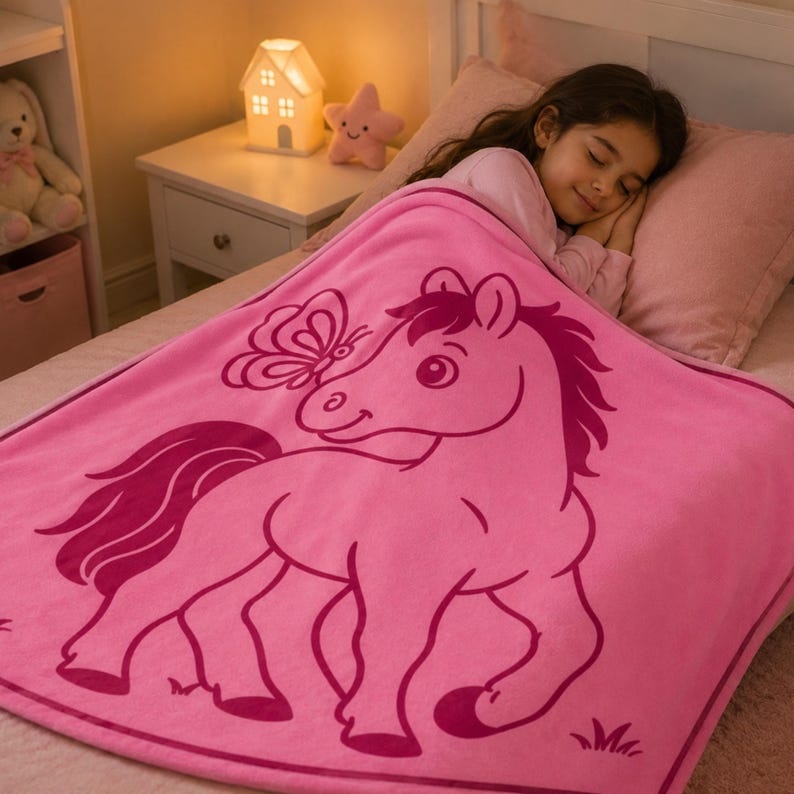 May include: A pink blanket with a cartoon horse and butterfly design. The blanket covers a bed, with a sleeping child visible. A nightstand with a house-shaped lamp and star-shaped light is in the background.