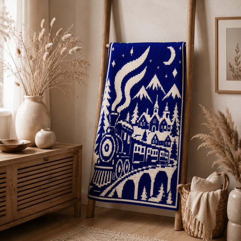 May include: A rectangular crochet blanket featuring a deep blue and white color scheme. The design depicts a steam train traveling across a bridge toward a village with mountains, a crescent moon, and stars in the night sky above the scene.