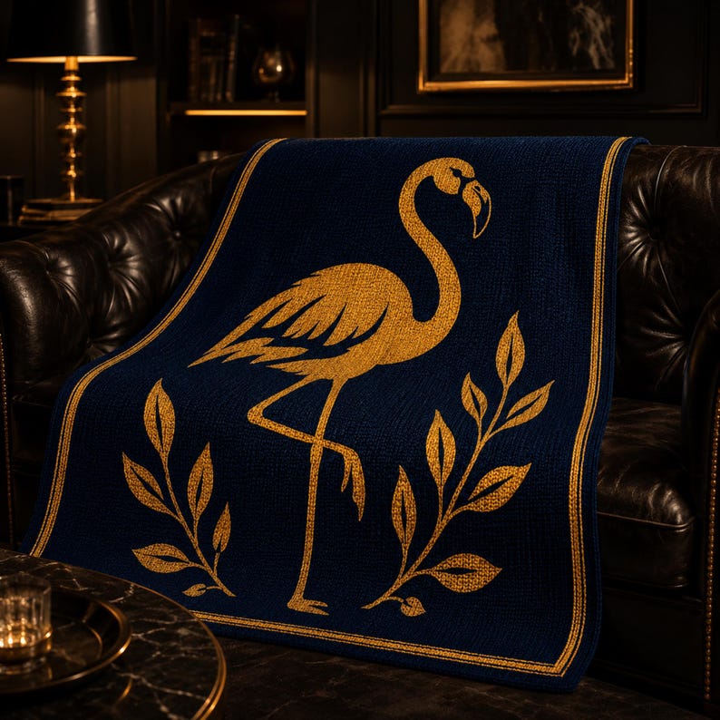 Peut inclure: Une couverture bleu marine avec un motif de flamant rose dor&eacute;. La couverture pr&eacute;sente une bordure dor&eacute;e et des accents de feuilles dor&eacute;es. Le jet&eacute; est drap&eacute; sur un canap&eacute; en cuir marron fonc&eacute;, cr&eacute;ant un accent luxueux et d&eacute;coratif.