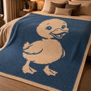 May include: A blue and beige crocheted blanket featuring a large cartoon duck design. The duck is beige, and the blanket's background is blue with a beige border. The blanket is displayed on a bed.