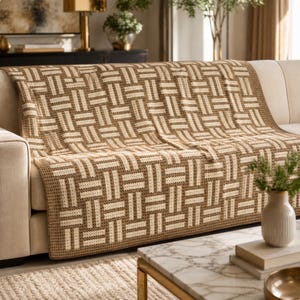 May include: A beige and cream-colored woven throw blanket with a geometric pattern is draped over a beige sofa. The blanket features a repeating rectangular design. The sofa is in a living room setting with a marble coffee table and decorative items.