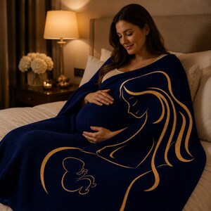 May include: A navy blue blanket with a gold illustration of a mother and child. The blanket is wrapped around a pregnant person. The scene is softly lit by a lamp and a candle, creating a warm atmosphere.