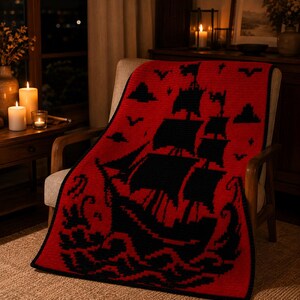 May include: A rectangular crochet blanket featuring a bold red background with a large black graphic of a sailing ship on the ocean. The design includes black silhouettes of birds and clouds in the sky, all bordered by a thin black edge.