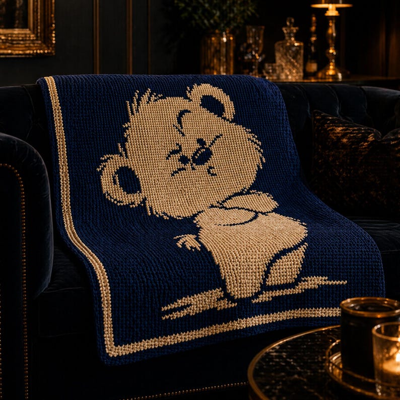 May include: A navy blue knitted throw blanket with a tan cartoon bear design. The blanket has a tan border and is draped over a dark blue sofa. The bear is in a seated position with its arms crossed.