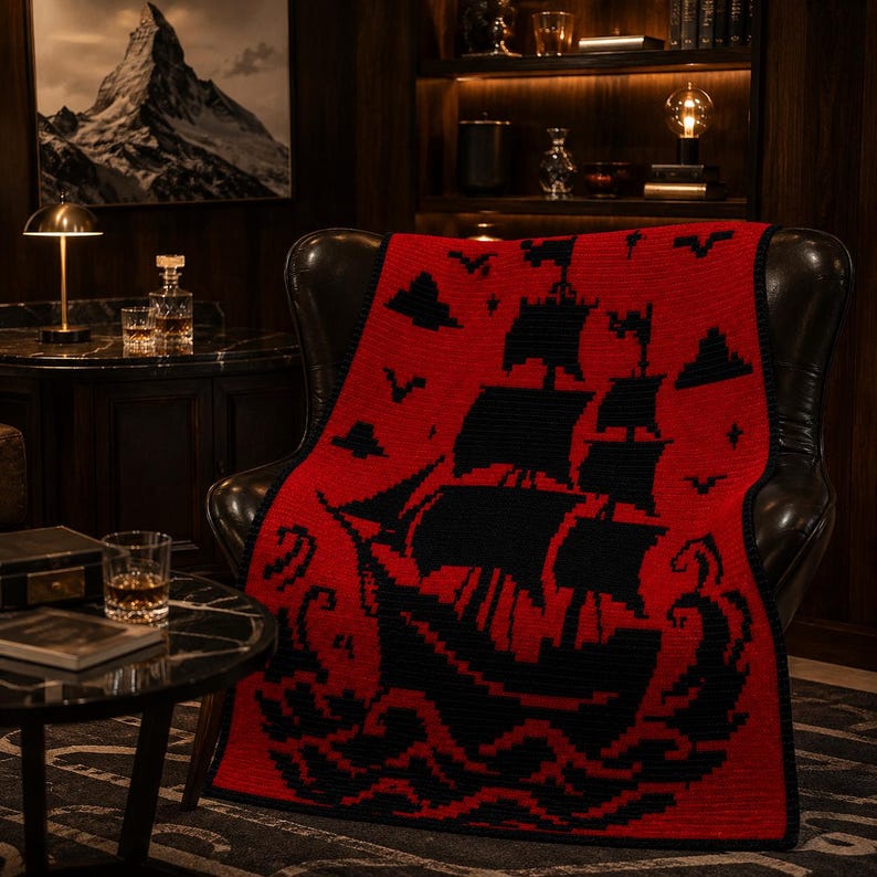 May include: A rectangular knit blanket featuring a bold red background with a large black graphic of a sailing ship on turbulent waves. The design includes black silhouettes of birds and clouds in the sky, finished with a solid black border.