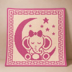May include: A pink and cream-colored crocheted baby blanket. The blanket features a pink elephant sitting on a crescent moon, surrounded by stars. A pink border with a Greek key design frames the image.