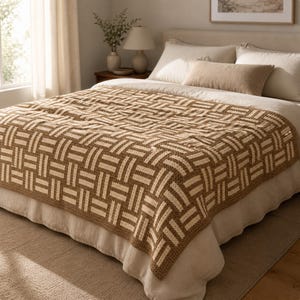 May include: A woven blanket with a geometric pattern in shades of brown and cream, draped over a bed. The blanket's design features a repeating rectangular motif, creating a textured appearance. The bed is made with white sheets and pillows, and the room has a neutral color palette.