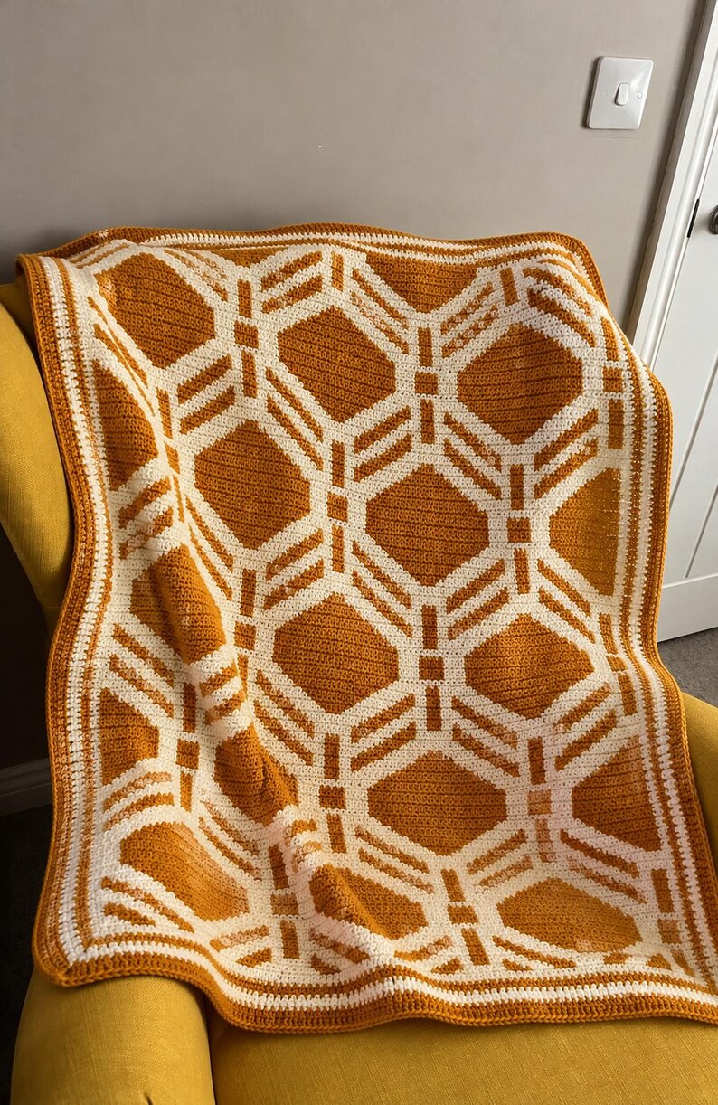 May include: A crochet blanket featuring a repeating geometric pattern of white lines on a mustard yellow background. The design consists of interconnected diamond and square shapes, finished with a simple white and yellow border.