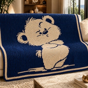 May include: A navy blue knitted throw blanket with a light tan bear design. The bear is smiling and has a bow tie. The blanket has a light tan border and is draped over a sofa. The blanket measures approximately 150 cm x 180 cm.