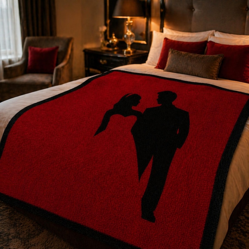Pode incluir: Um cobertor vermelho com uma borda preta e uma silhueta de um casal. O cobertor est&aacute; em uma cama com len&ccedil;&oacute;is brancos e almofadas vermelhas. O quarto tem uma est&eacute;tica escura e elegante.