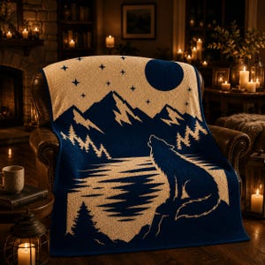 May include: A navy blue and cream-colored throw blanket featuring a woven graphic of a wolf howling at a full moon. The design includes a mountain range, a forest of pine trees, and a starry night sky, all rendered in a two-tone color scheme.