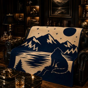 May include: A rectangular woven throw blanket featuring a dark blue and cream color scheme. The design depicts a wolf howling at a full moon above a mountain range, a forest of pine trees, and a lake. The blanket is draped over a leather sofa.
