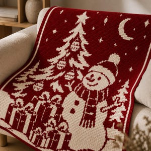 May include: A deep red and cream-colored crocheted blanket featuring a repeating pixelated pattern of a snowman wearing a hat and scarf, a decorated Christmas tree, wrapped gift boxes, a crescent moon, and small stars across the fabric surface.