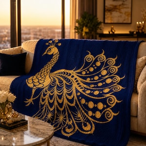 May include: A navy blue throw blanket featuring a gold peacock design. The peacock is depicted with intricate detailing, including a fanned tail and a crown. The blanket is draped over a beige sofa, creating a decorative accent.