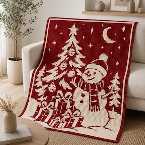 May include: A rectangular crochet blanket featuring a deep red background with a cream-colored pattern. The design displays a decorated Christmas tree, a snowman wearing a hat and scarf, wrapped gift boxes, and a crescent moon with stars.