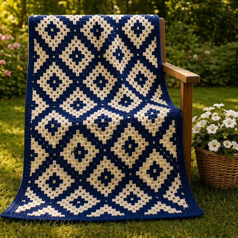 May include: A navy blue and cream crocheted blanket with a diamond pattern is draped over a wooden chair. The blanket's design features alternating squares of navy blue and cream, creating a textured look. This blanket is a cozy home decor item, perfect for a living room.