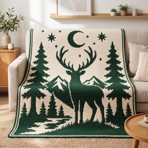Peut inclure: Une couverture en crochet rectangulaire pr&eacute;sentant un motif vert fonc&eacute; et cr&egrave;me. Le design affiche la silhouette centrale d'un cerf devant des montagnes, encadr&eacute; par de grands pins, avec un croissant de lune et des &eacute;toiles au-dessus.