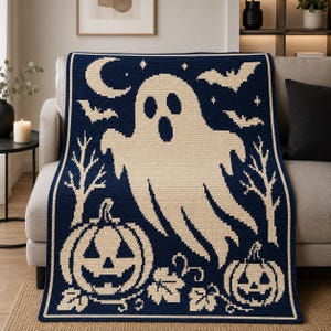 May include: A rectangular crochet blanket featuring a dark navy blue background with a cream-colored pattern. The design includes a large central ghost, two jack-o'-lantern pumpkins, bare trees, flying bats, a crescent moon, and small stars.