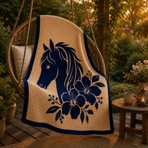 May include: A tan throw blanket with a navy blue horse head and floral design. The blanket has a navy blue border and is draped over a wicker chair. The blanket is made of a soft, textured material.