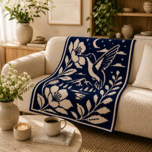 May include: A rectangular throw blanket featuring a dark blue and cream color scheme. The design displays a central hummingbird hovering near a large flower, surrounded by foliage, a crescent moon, stars, and a mountain landscape at the bottom.