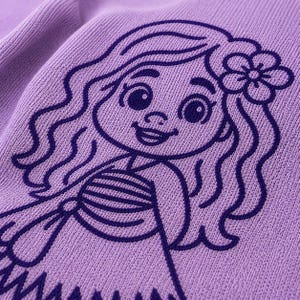 May include: A close-up of a lilac-colored fabric with a detailed embroidered design of a cartoon mermaid. The mermaid has long wavy hair, a flower in her hair, and a smiling expression. The design is in a darker shade of purple.