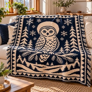 May include: A navy blue and cream-colored woven throw blanket featuring a central owl perched on a pine branch, surrounded by pine trees and snowflakes, with a decorative geometric border and fringed edges on the sides.