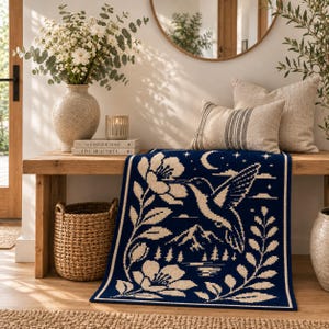 May include: A rectangular woven textile runner featuring a dark navy blue background with a cream-colored graphic pattern. The design depicts a hummingbird hovering near large flowers, with a mountain range, a crescent moon, and stars.
