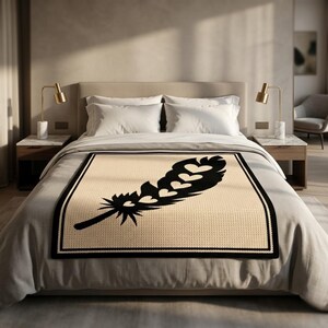 May include: A beige blanket with a large black feather design featuring heart shapes. The blanket has a black border and is placed on a bed with white bedding. Two gold lamps sit on bedside tables.