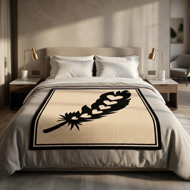 May include: A beige blanket with a large black feather design featuring heart shapes. The blanket has a black border and is placed on a bed with white bedding. Two gold lamps sit on bedside tables.
