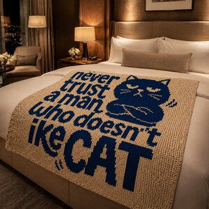 May include: Beige knitted throw blanket with a navy blue cat graphic and text that reads "Never trust a man who doesn't like CAT". The blanket is folded over a bed with white sheets and pillows.