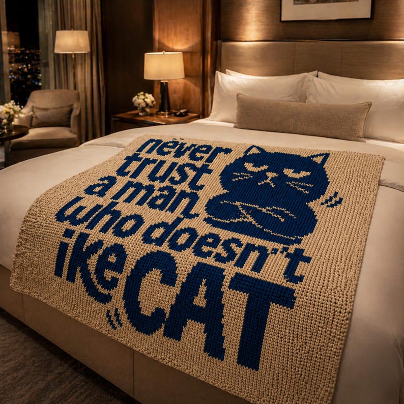 May include: Beige knitted throw blanket with a navy blue cat graphic and text that reads "Never trust a man who doesn't like CAT". The blanket is folded over a bed with white sheets and pillows.