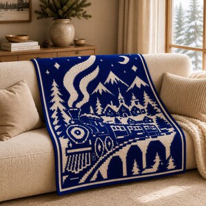 May include: A rectangular knit throw blanket featuring a deep blue background with a contrasting white graphic design. The pattern depicts a steam locomotive traveling across a bridge toward a village with mountains, pine trees, stars, and a crescent moon.