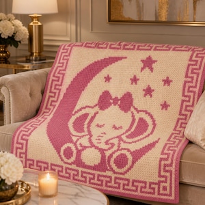 May include: A pink and cream-colored crochet baby blanket featuring an elephant design. The elephant is nestled on a crescent moon, surrounded by stars. The blanket has a decorative border and is draped over a sofa.