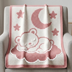 May include: A rectangular crochet blanket featuring a cream-colored base with a dusty rose border. The design displays a sleeping bear resting on a cloud, surrounded by a crescent moon and four stars, all rendered in a matching dusty rose yarn.